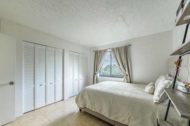 bedroom with multiple closets, a textured ceiling, and light tile patterned floors