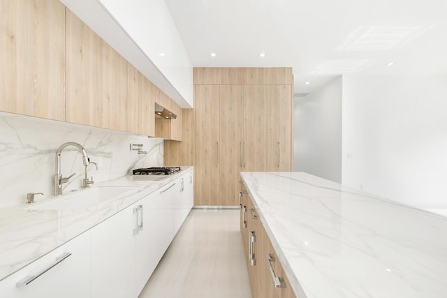 kitchen featuring light stone countertops, light brown cabinetry, stainless steel gas cooktop, sink, and white cabinetry