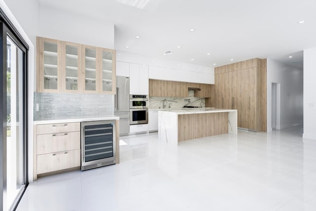 kitchen with backsplash, stainless steel appliances, beverage cooler, a center island, and white cabinetry