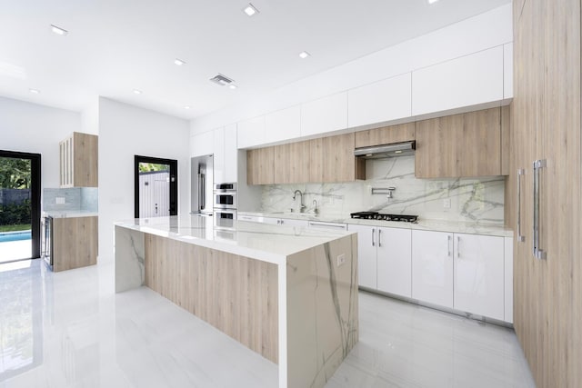 kitchen with white cabinets, ventilation hood, sink, a kitchen island, and light stone counters