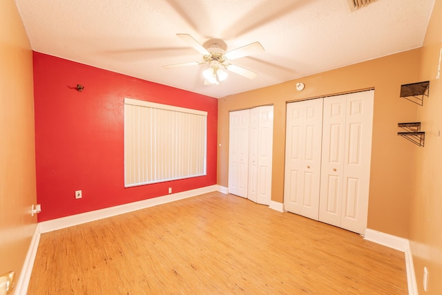 unfurnished bedroom featuring ceiling fan, two closets, and light hardwood / wood-style flooring