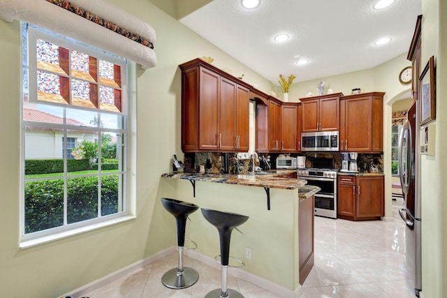 kitchen featuring light tile patterned floors, appliances with stainless steel finishes, kitchen peninsula, and a healthy amount of sunlight