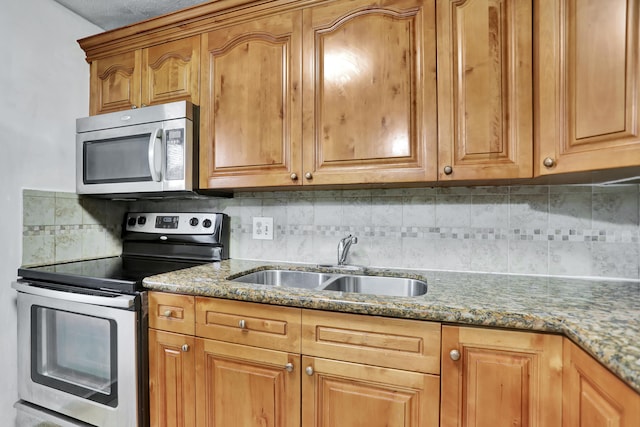 kitchen with appliances with stainless steel finishes, sink, tasteful backsplash, and dark stone countertops