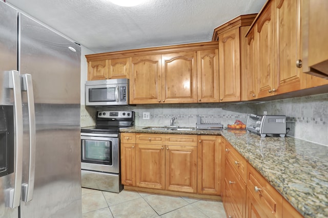 kitchen featuring light tile patterned floors, appliances with stainless steel finishes, stone countertops, sink, and backsplash