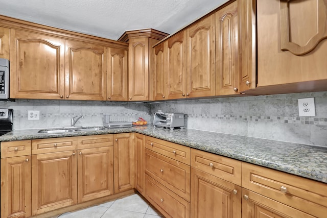 kitchen with a textured ceiling, light tile patterned flooring, backsplash, light stone counters, and sink