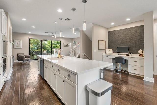 kitchen with white cabinets, hanging light fixtures, dark wood-type flooring, a center island with sink, and sink