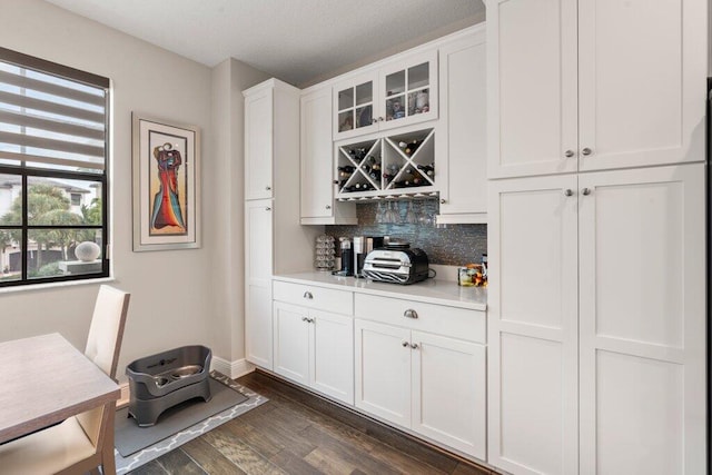 bar with dark hardwood / wood-style floors, white cabinetry, and backsplash