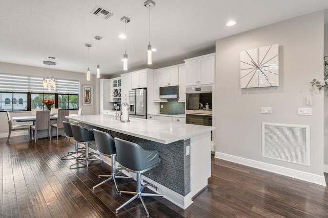 kitchen with stainless steel appliances, an island with sink, white cabinets, dark wood-type flooring, and a kitchen bar