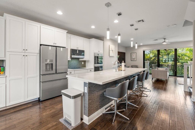 kitchen featuring ceiling fan, appliances with stainless steel finishes, a kitchen island with sink, tasteful backsplash, and dark hardwood / wood-style flooring