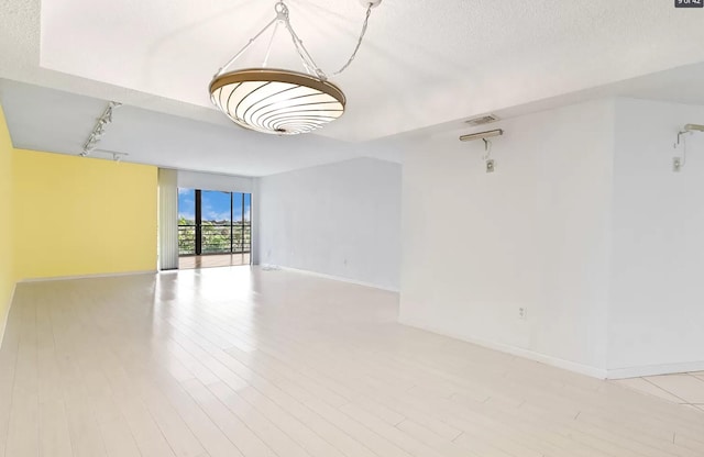 empty room featuring a textured ceiling, track lighting, and light wood-type flooring