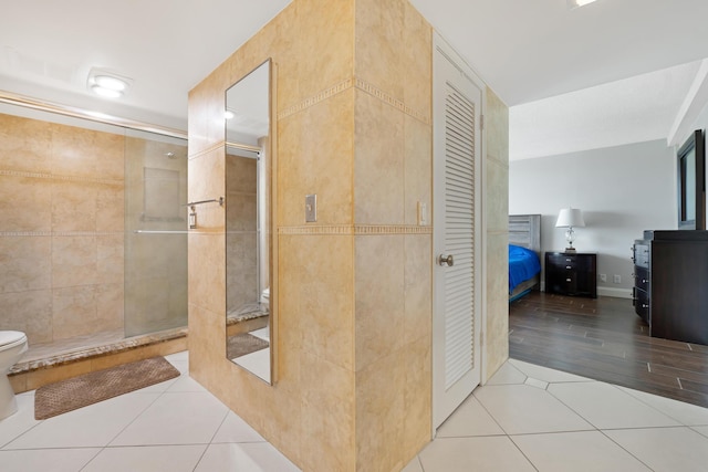 ensuite bathroom featuring tile patterned flooring, a shower stall, tile walls, toilet, and ensuite bath