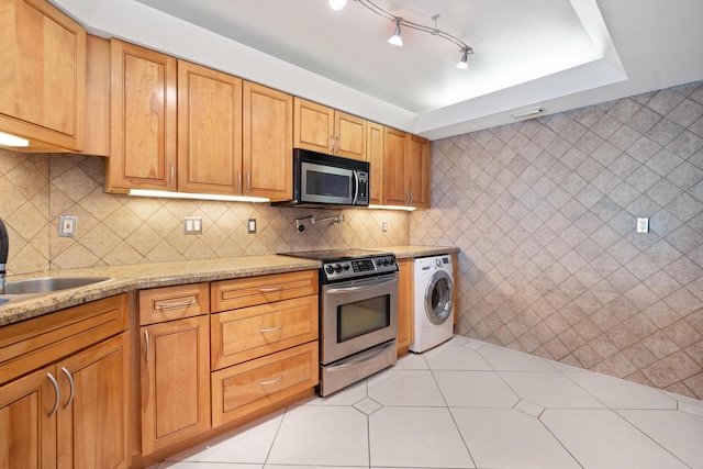 kitchen with light tile patterned floors, washer / dryer, appliances with stainless steel finishes, and backsplash