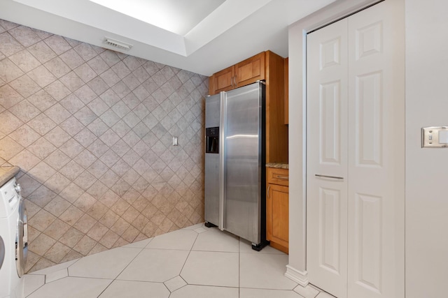 kitchen with light tile patterned floors, washer / dryer, stainless steel fridge with ice dispenser, tile walls, and brown cabinets