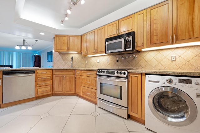 kitchen with a sink, backsplash, stainless steel appliances, light tile patterned flooring, and washer / dryer