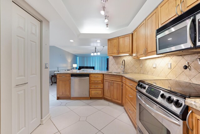 kitchen with tasteful backsplash, light stone counters, a peninsula, stainless steel appliances, and a sink