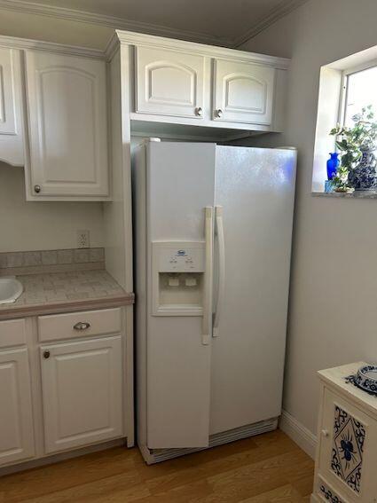 kitchen featuring white refrigerator with ice dispenser, light hardwood / wood-style floors, white cabinets, and crown molding