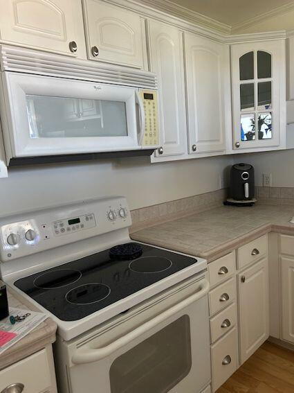 kitchen with white cabinets, light hardwood / wood-style flooring, and white appliances