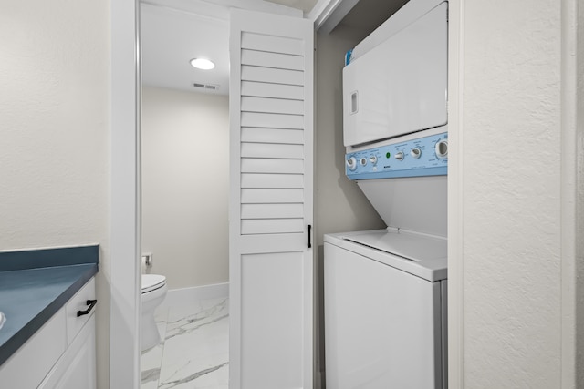 laundry room featuring laundry area, visible vents, baseboards, marble finish floor, and stacked washing maching and dryer