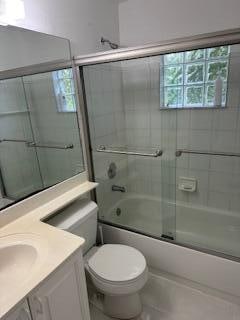 full bathroom featuring vanity, toilet, and shower / bath combination with glass door