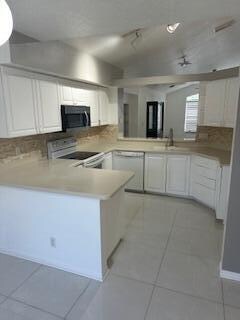 kitchen with white cabinets, black appliances, sink, light tile patterned floors, and kitchen peninsula