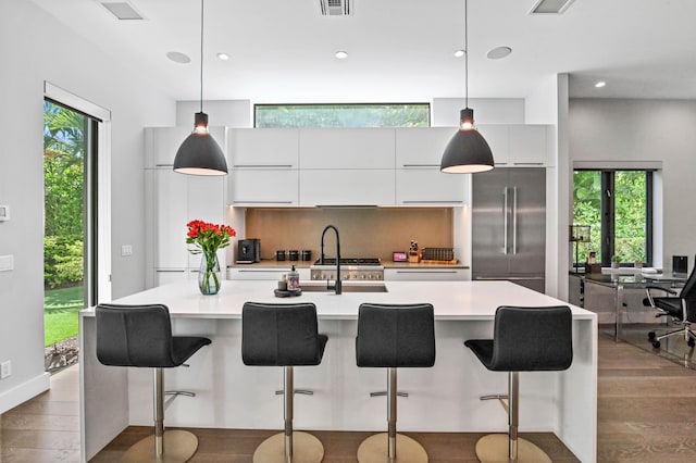 kitchen with white cabinets, pendant lighting, high quality fridge, and an island with sink