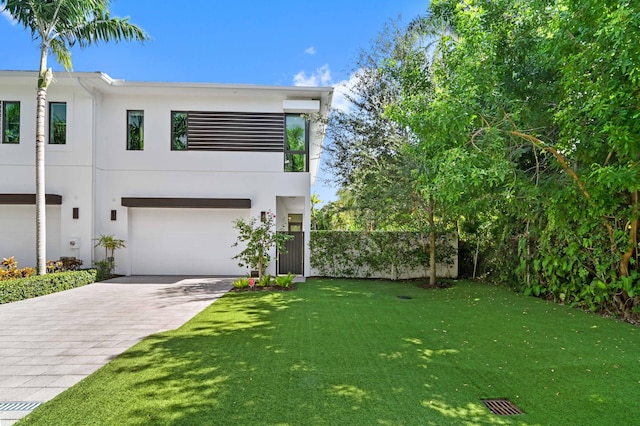 contemporary house featuring a garage, fence, decorative driveway, a front lawn, and stucco siding