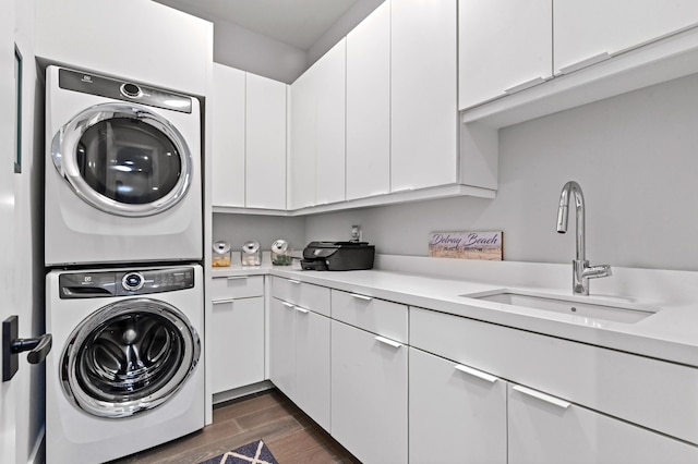 clothes washing area with stacked washer and dryer, cabinet space, a sink, and wood finish floors