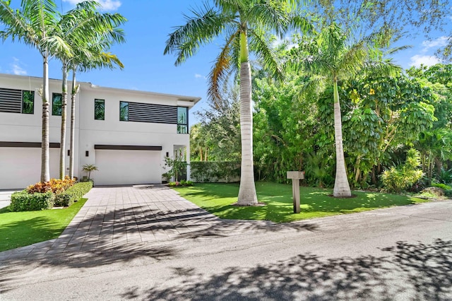 contemporary house featuring decorative driveway, an attached garage, a front lawn, and stucco siding