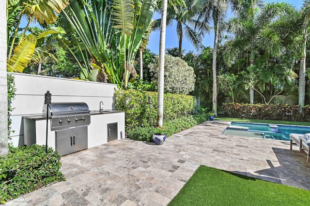 view of patio with area for grilling, a fenced in pool, sink, and grilling area