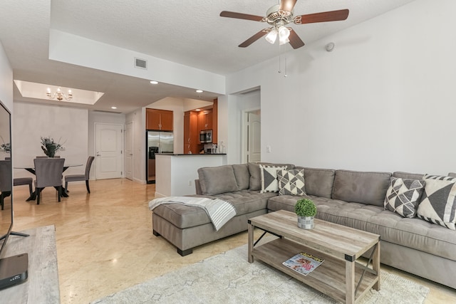 tiled living room featuring ceiling fan with notable chandelier, a textured ceiling, and a tray ceiling