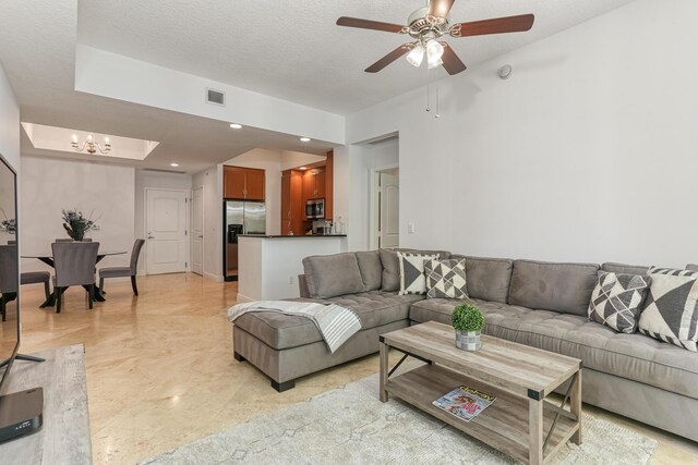 living room featuring ceiling fan with notable chandelier and a textured ceiling