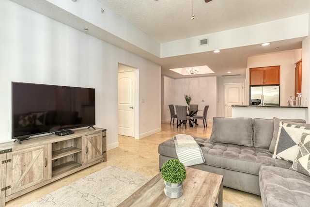 tiled living room with ceiling fan with notable chandelier and a textured ceiling