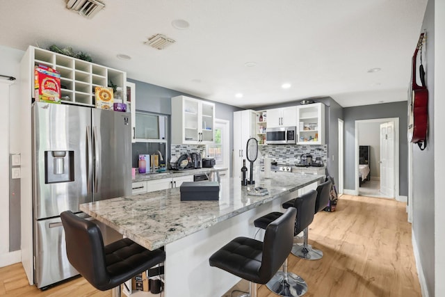 kitchen featuring stainless steel appliances, decorative backsplash, white cabinets, a breakfast bar area, and light hardwood / wood-style flooring