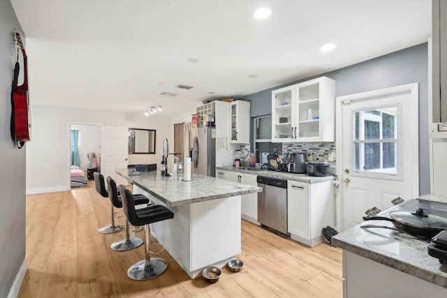 kitchen with appliances with stainless steel finishes, white cabinets, a breakfast bar area, and light stone countertops