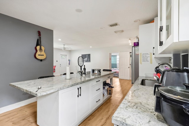 kitchen with white cabinetry, light hardwood / wood-style flooring, light stone counters, and a kitchen island