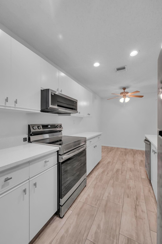 kitchen with appliances with stainless steel finishes, light hardwood / wood-style flooring, white cabinets, and ceiling fan