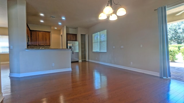 unfurnished living room with an inviting chandelier and dark hardwood / wood-style flooring