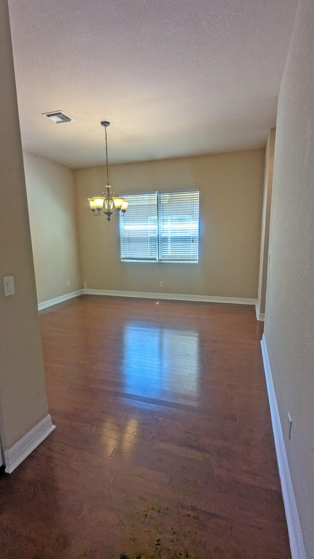 spare room with dark hardwood / wood-style floors and a chandelier