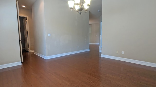 spare room featuring a chandelier and dark wood-type flooring