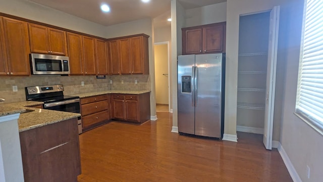 kitchen featuring dark wood-type flooring, light stone counters, stainless steel appliances, and tasteful backsplash