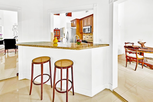 kitchen featuring light tile patterned floors, stone counters, stainless steel appliances, decorative backsplash, and kitchen peninsula