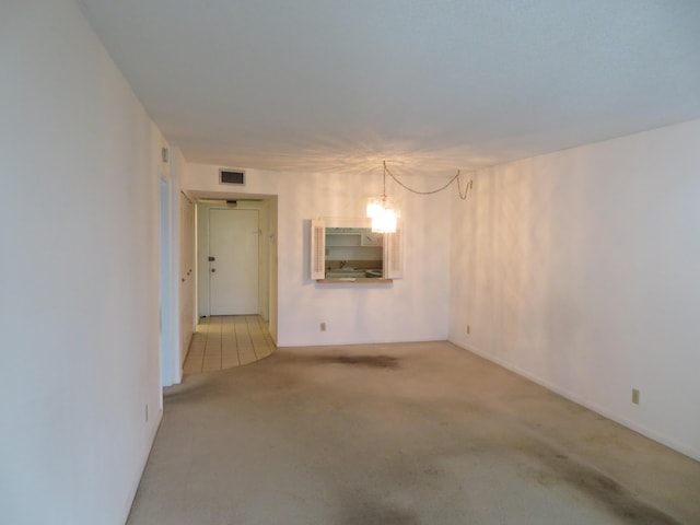 carpeted empty room featuring an inviting chandelier