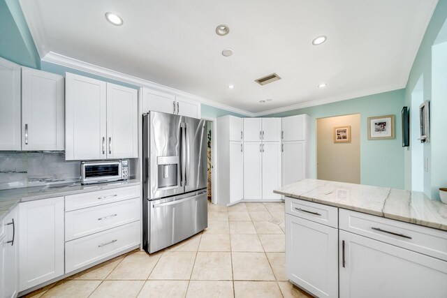 kitchen with backsplash, white cabinetry, light stone counters, ornamental molding, and stainless steel fridge