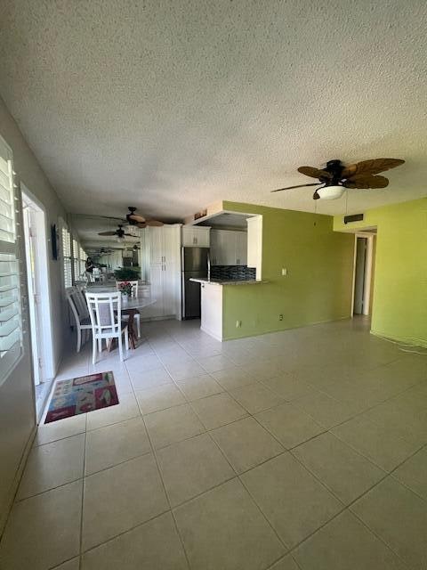 unfurnished living room featuring a textured ceiling, light tile patterned floors, and ceiling fan