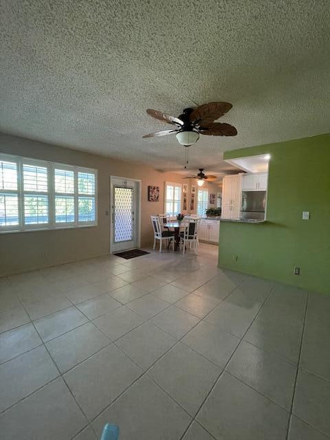 interior space with a textured ceiling, light tile patterned flooring, and ceiling fan