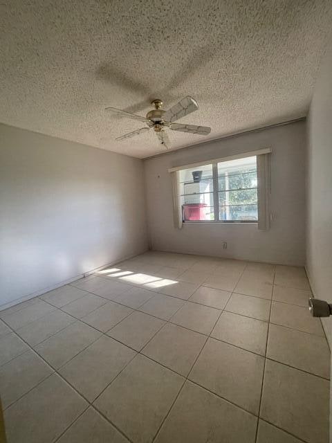 tiled empty room featuring ceiling fan and a textured ceiling