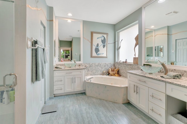 bathroom featuring a sink, two vanities, visible vents, a jetted tub, and a shower stall