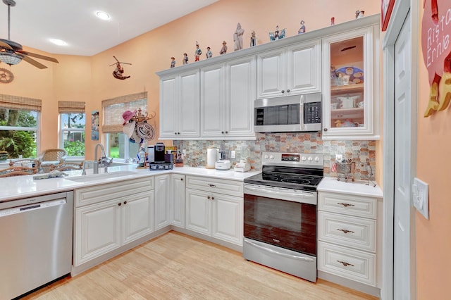 kitchen with light countertops, appliances with stainless steel finishes, glass insert cabinets, white cabinetry, and a sink