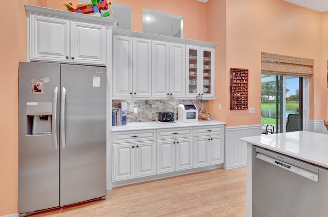 kitchen featuring appliances with stainless steel finishes, white cabinets, light wood-type flooring, and tasteful backsplash