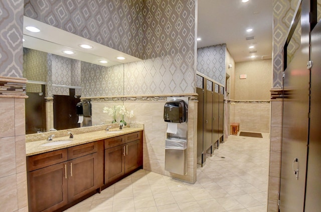 bathroom with double vanity, wallpapered walls, tile walls, and a sink